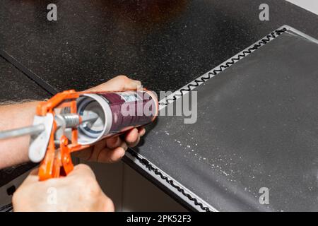 L'idraulico installa il lavello. Applicazione del sigillante sul bordo di un lavello da cucina per l'installazione sul piano di appoggio. Foto Stock