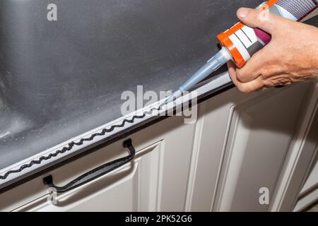 L'idraulico installa il lavello. Applicazione del sigillante sul bordo di un lavello da cucina per l'installazione sul piano di appoggio. Foto Stock