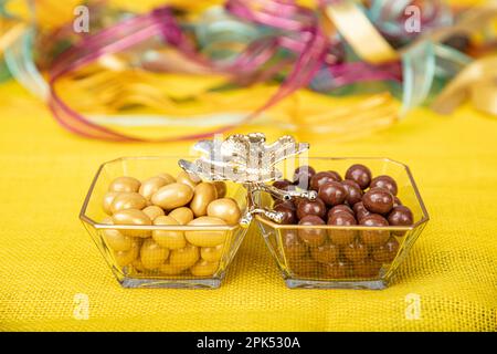 Drago di nocciola rivestito di cioccolato. Mandorle ricoperte di cioccolato fondente in un recipiente di vetro. Drago al cioccolato su tavolo di legno. Foto Stock