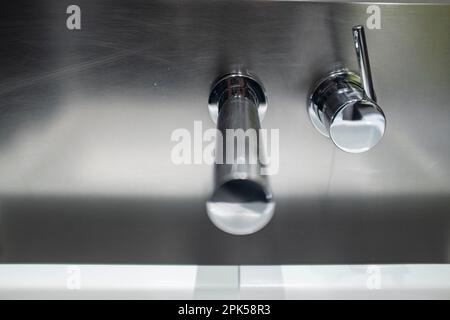 Rubinetto d'acqua in argento dal design moderno su una parete cromata Foto Stock