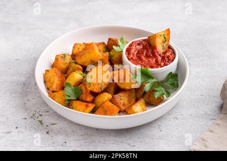 Patata tradizionale spagnola, patata bravas con paprika affumicata, salsa di pomodoro piccante e prezzemolo in una ciotola bianca su sfondo di pietra grigia, vista dall'alto. D Foto Stock