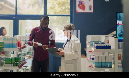 Cliente maschile con carta da prescrizione chiedendo specialista circa il trattamento, cercando di acquistare farmaci e vitamine da scaffali farmacia. Caselle di controllo dei supplementi in farmacia. Foto Stock