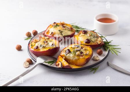 Pesche al forno con formaggio blu, nocciole, rosmarino, servite con miele su sfondo grigio chiaro Foto Stock