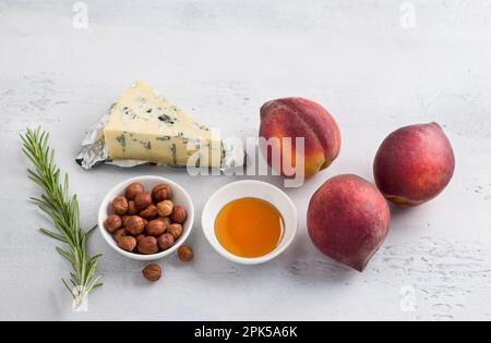 Ingredienti per pesche al forno: Pesche fresche, formaggio azzurro, nocciole, miele e rosmarino su sfondo grigio chiaro, vista dall'alto Foto Stock