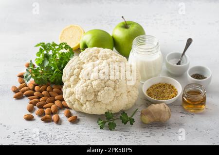 Ingredienti per insalate vegetali: Cavolfiore, mele, limone, mandorle, prezzemolo, yogurt, zenzero, senape, sale, pepe nero e aceto di vino su un blu chiaro Foto Stock