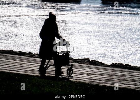Donna anziana che cammina lungo un fiume con un rollator, Foto Stock