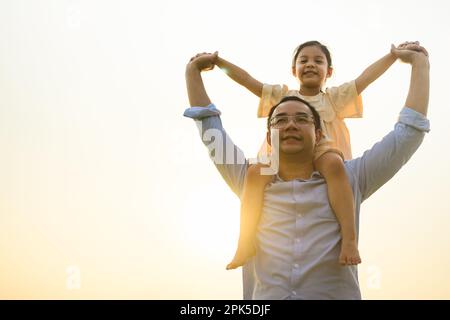 Felice padre che dà la figlia piggyback sulla spalla con vista del tramonto Foto Stock