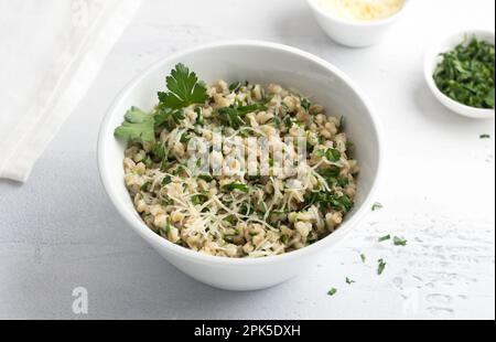 Orzo perlato con formaggio ed erbe in ciotola di ceramica bianca su sfondo grigio chiaro, vista dall'alto. Colazione deliziosa e sana Foto Stock