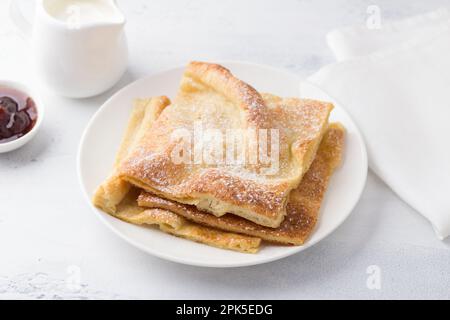 Un piatto di tradizionali pancake finlandesi o danesi pannukakku cosparso di zucchero a velo con panna acida e marmellata su sfondo chiaro. Delizioso ve Foto Stock