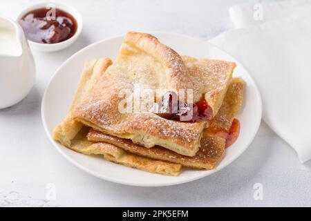 Un piatto di tradizionali pancake finlandesi o danesi pannukakku cosparso di zucchero a velo con panna acida e marmellata su sfondo chiaro. Delizioso ve Foto Stock