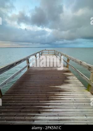 Vuoto molo di legno per il Ria de Aveiro in Portogallo, con cielo drammatico e acqua calma. Torreira, Murtosa - Portogallo. Foto Stock