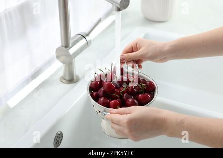 Donna lavaggio ciliegie fresche mature sotto acqua corrente in cucina, primo piano Foto Stock