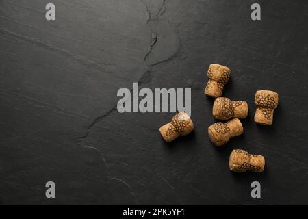 Tappi di vino frizzante con immagini d'uva su tavola nera, giacitura piatta. Spazio per il testo Foto Stock