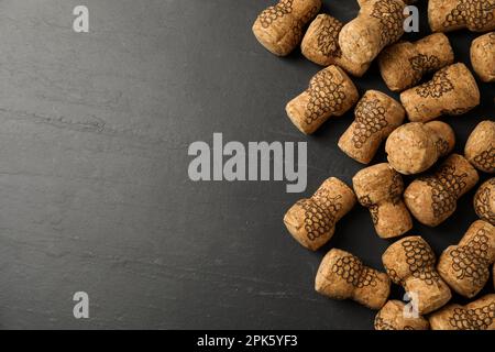 Tappi di vino frizzante con immagini d'uva su tavola nera, giacitura piatta. Spazio per il testo Foto Stock