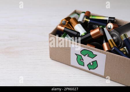 Batterie usate in una scatola di cartone con il simbolo di riciclaggio sul tavolo bianco, primo piano. Spazio per il testo Foto Stock