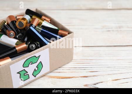 Batterie usate in scatola di cartone con il simbolo di riciclaggio su un tavolo di legno bianco, primo piano. Spazio per il testo Foto Stock