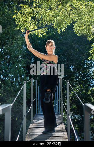 Donna pratica spada tai chi su un ponte. La spada tai chi è uno strumento importante in questa pratica, in quanto viene utilizzata per aumentare la concentrazione e la p Foto Stock