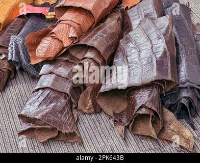 Pellicce, pelli di coccodrillo sono viste arrotolate in su per la vendita in fasci di tessuto dopo che sono state conciate & tinte. I colori dei materiali sono marrone, marrone, nero. Foto Stock