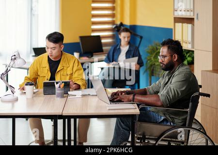 Uomo con disabilità che lavora in ufficio con diversi team aziendali Foto Stock
