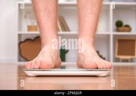 Un uomo si trova sulla bilancia. Il ragazzo sta pesando se stesso. Bilance da pavimento per la salute. Controllo del peso. Foto Stock