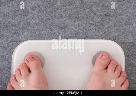 Un uomo si trova sulla bilancia. Il ragazzo sta pesando se stesso. Bilance da pavimento per la salute. Controllo del peso. Foto Stock