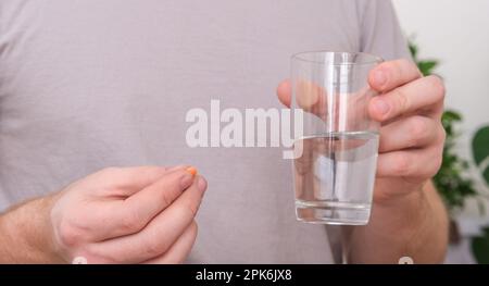 Uomo caucasico che prende una pillola e beve un bicchiere d'acqua. Giovane uomo che prende la vitamina all'interno. Salute, medicina, concetto di trattamento. Foto Stock