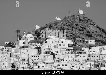 Vista panoramica di una chiesa, cappelle più piccole e la bandiera greca sulla cima di una collina che domina il Mar Egeo a iOS in Grecia, noto anche come Chora Foto Stock