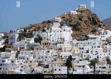 Vista panoramica di una chiesa, cappelle più piccole e la bandiera greca sulla cima di una collina che domina il Mar Egeo a iOS in Grecia, noto anche come Chora Foto Stock