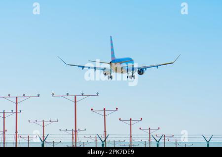 Primo piano di un grande aereo passeggeri che si prepara ad atterrare come visto da dietro sopra i lampioni sulla pista con un cielo blu chiaro. Foto Stock