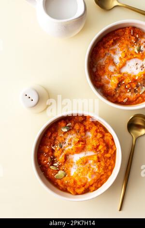 Pranzi salutari, deliziosa zuppa di crema di zucca su sfondo giallo, zuppa con girasole e semi di zucca, sesamo e lino e latte di cocco Foto Stock