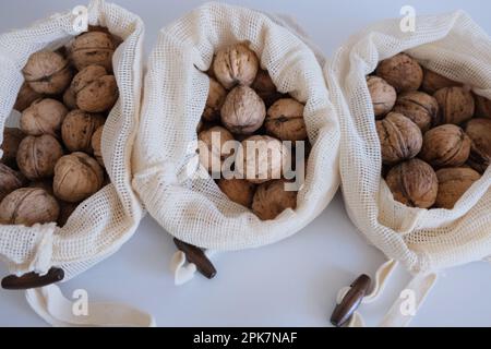 Noci sgusciate, mucchio di noci sgusciate in tre sacchetti di stoffa bianca su fondo bianco affiancati. Sacchetti di stoffa pieni di concetto di noci sgusciate. Foto Stock