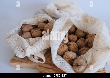 Noci sgusciate, mucchio di noci con sgusciate in sacchi di stoffa bianca su fondo bianco con tagliere di legno. Foto Stock