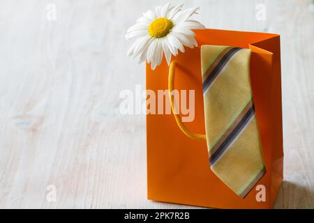 Il concetto del giorno dei padri con cravatta e fiore in borsa regalo su sfondo chiaro Foto Stock