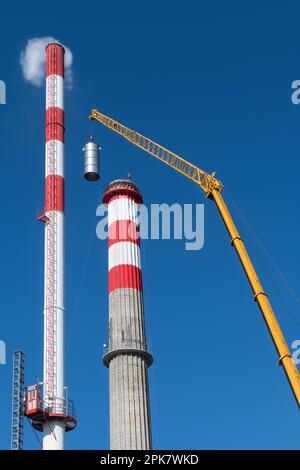 Alto camino da fumo e rinnovatore con braccio gru su sfondo blu cielo. Braccio macchina paranco giallo sul posizionamento del rivestimento interno del camino durante la riparazione del sacco. Foto Stock