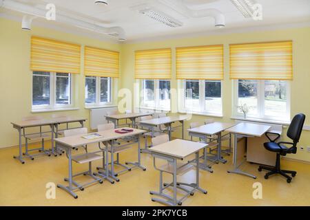 Un'aula scolastica con scrivanie e sedie e tende per finestre gialle. Foto Stock