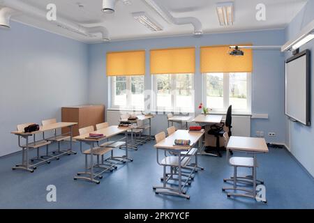 Un'aula scolastica con scrivanie e sedie e tende per finestre gialle. Foto Stock