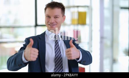 Uomo d'affari di successo in tuta mostrando pollici in ufficio Foto Stock