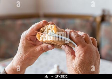 Anziana pensionato granny si siede al tavolo fisso per la colazione mangiando un rotolo coperto di banconote in euro, Germania Foto Stock