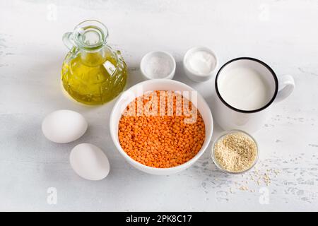 Ingredienti per un piatto vegetariano, pane di lenticchie, pancake, casseruole: Lenticchie rosse, yogurt, olio d'oliva, uova, semi di sesamo, lievito in polvere e sale su un Foto Stock