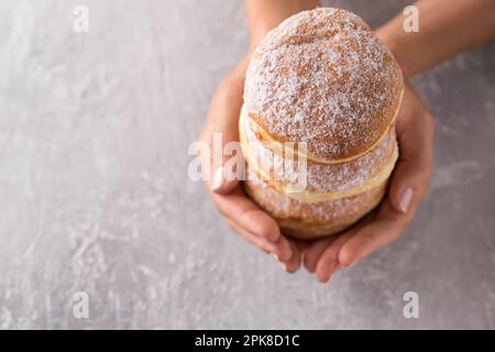 Tre ciambelle in mani femminili su sfondo grigio Foto Stock