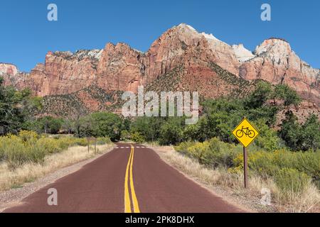 Zion Canyon Park Road che si snoda attraverso una vegetazione lussureggiante con alberi di Cottonwood ai piedi delle ripide scogliere di arenaria Navajo che torreggiano sulla valle Foto Stock