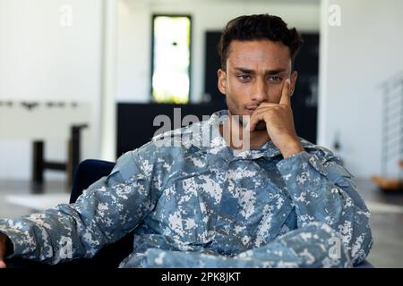 Preoccupato soldato biraciale maschio indossando uniforme militare, seduto in poltrona nel soggiorno di casa. Stile di vita, servizio militare e tempo libero, inalterabile Foto Stock