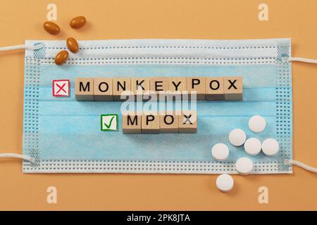 I nomi del virus Monkeypox e Mpox sono rivestiti con cubi di legno su una maschera chirurgica. Il nuovo nome corretto MPOX è contrassegnato da un segno di spunta verde, Foto Stock