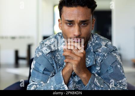 Preoccupato soldato biraciale maschio indossando uniforme militare, seduto in poltrona nel soggiorno di casa. Stile di vita, servizio militare e tempo libero, inalterabile Foto Stock