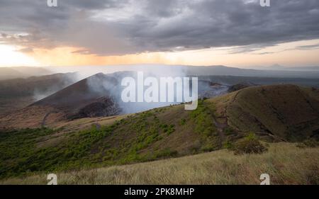 Paesaggio con vulcano attivo e fumo che si alza sullo sfondo del tramonto Foto Stock