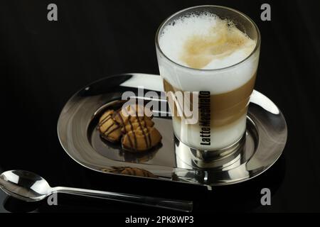 Un bicchiere di latte macchiato su un piatto con un piatto di biscotti. Foto Stock