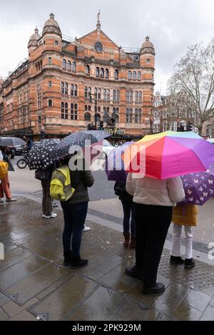 I turisti nel centro di Londra si rifugiano sotto gli ombrelloni davanti al Palace Theatre di Cambridge Circus, West End London, Inghilterra, Regno Unito Foto Stock