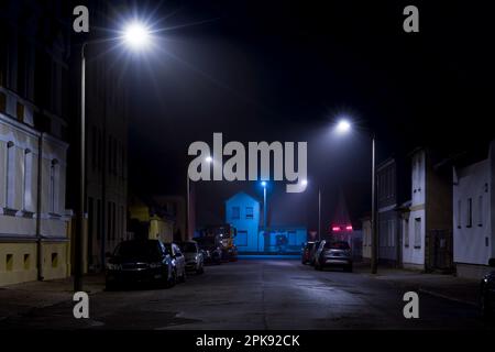 Di notte sulla strada, poca nebbia nella luce della lanterna, parcheggio auto sul lato della strada Foto Stock