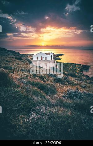 Piccola tipica chiesa greca direttamente sul mare, la cappella bianca di Agios Nikolaos su una costa rocciosa all'alba Foto Stock