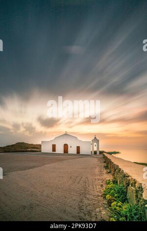 Piccola tipica chiesa greca direttamente sul mare, la cappella bianca di Agios Nikolaos su una costa rocciosa all'alba Foto Stock